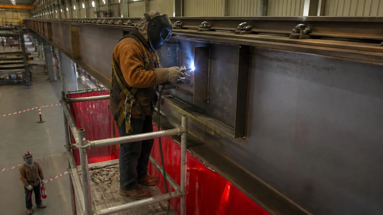 Welders adding steel cover plates and stiffeners to an overhead crane runway girder during a capacity upgrade